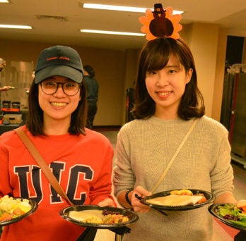 International students hold plates of Thanksgiving food.
                  