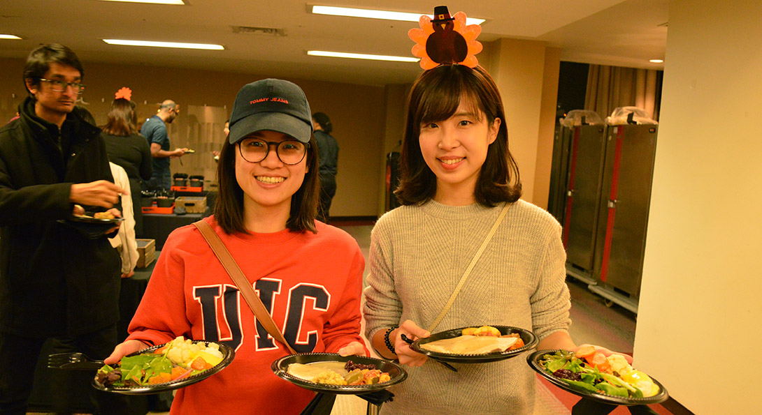 International students hold plates of Thanksgiving food.