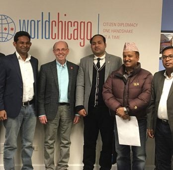 Eight men, inlcuding UIC Professor Dr. Evan McKenzie and senior delegates from India, Bangladesh, Nepal and Sri Lanka, pose and smile for a photo in front of a wall with the logo of Work Chicago.
                  