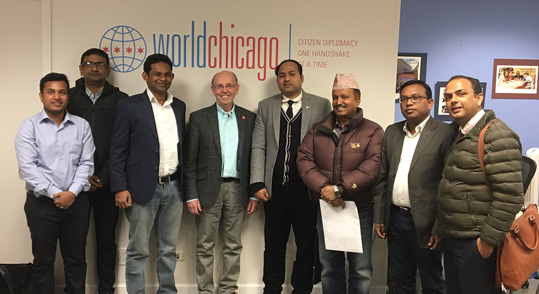 Eight men, inlcuding UIC Professor Dr. Evan McKenzie and senior delegates from India, Bangladesh, Nepal and Sri Lanka, pose and smile for a photo in front of a wall with the logo of Work Chicago.