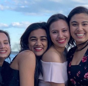 Four students hug and smile outside on a boat cruise of Lake Michigan.
                  