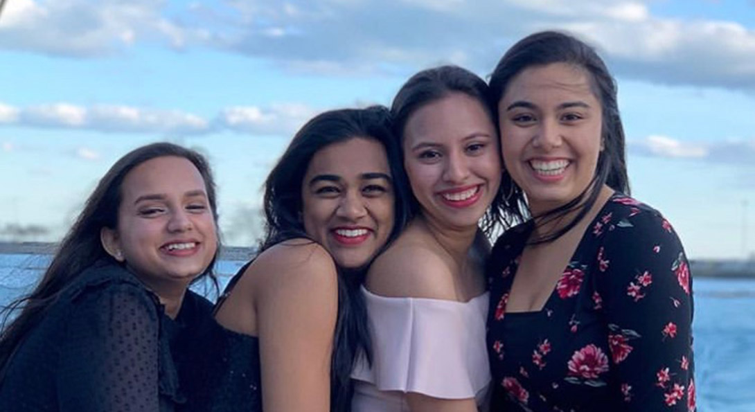 Four students hug and smile outside on a boat cruise of Lake Michigan.