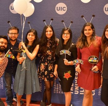 Seven students pose for a photo, smiling with while balloons and graduation headbands.
                  