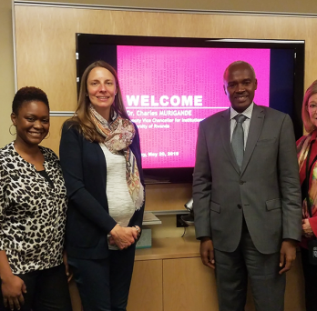 Five UIC faculty members stand with Ambassador Charles Murigande in front of a screen projecting the words 