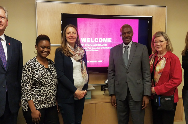 Five UIC faculty members stand with Ambassador Charles Murigande in front of a screen projecting the words 