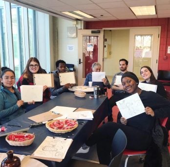 Seven students and faculty sitting holding up pieces of art they sketched
                  