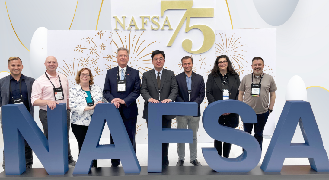 OGE administrators posing in front of NAFSA conference logo