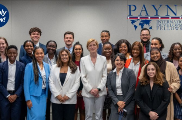 group of Payne Fellows from 2023 standing in front of the Payne Fellowship logo which is blue text on a light grey background