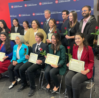 two rows of students holding red roses and their award certificates 
